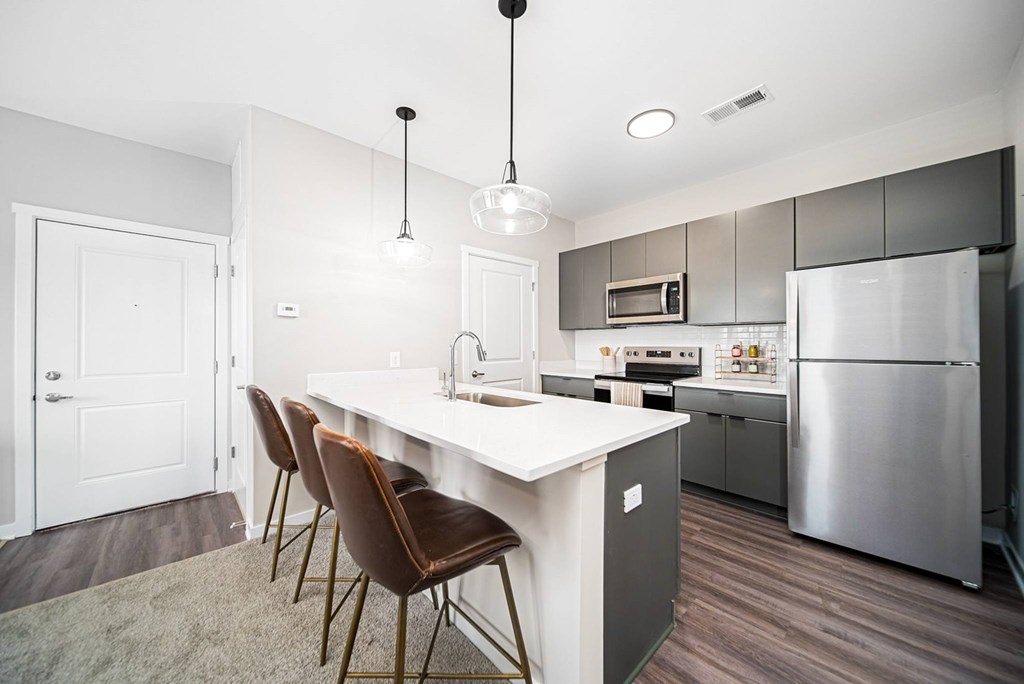 A modern kitchen with a white island and brown chairs.