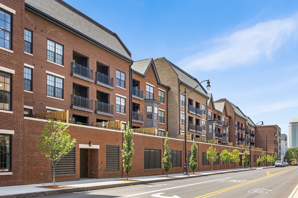 A row of red brick buildings with balconies and trees in front.
