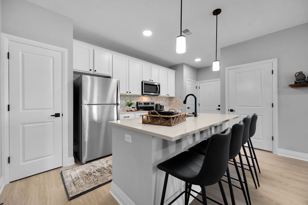 A kitchen with a white island and black chairs.