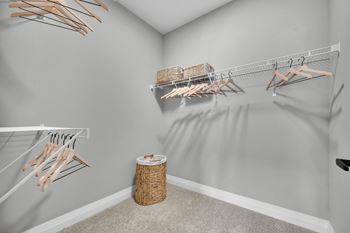 A room with a grey wall and a white shelf with clothes hangers.
