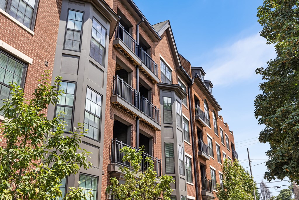 A red brick building with balconies and trees in front.
