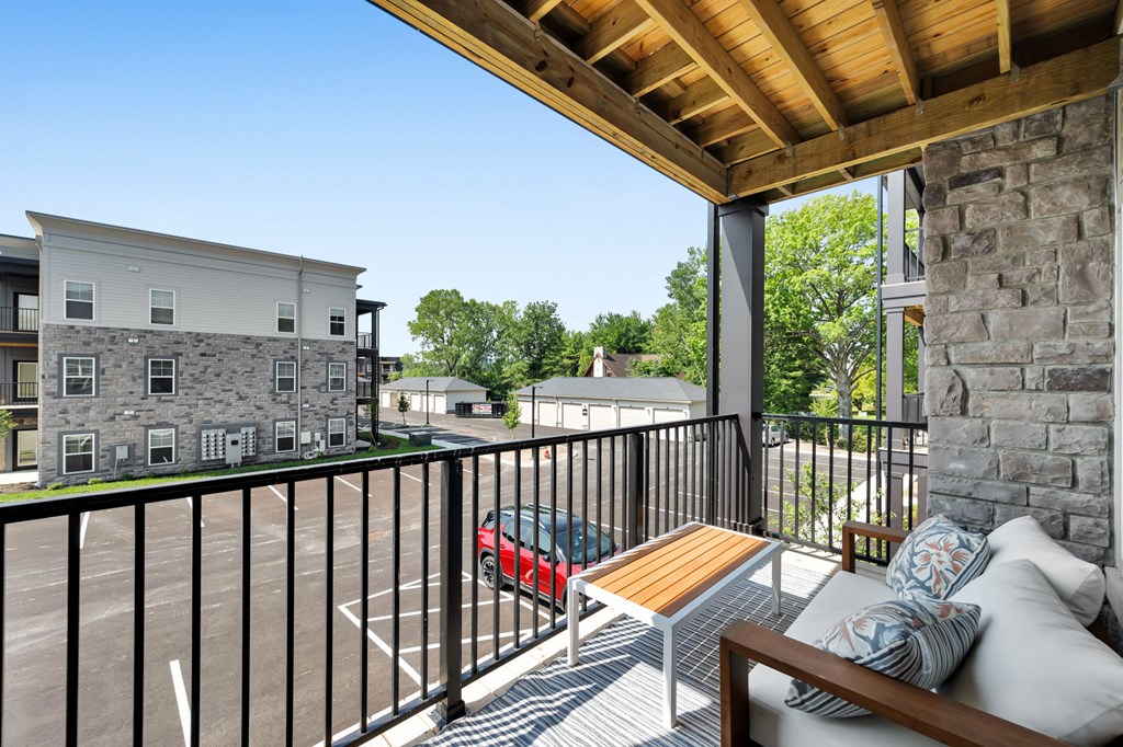 A balcony with a bench and pillows overlooks a parking lot.