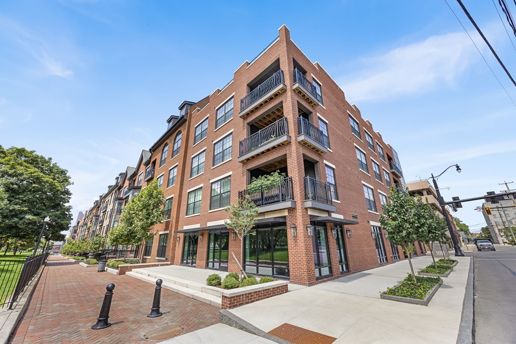 A red brick apartment building with a black fence and bushes in front.