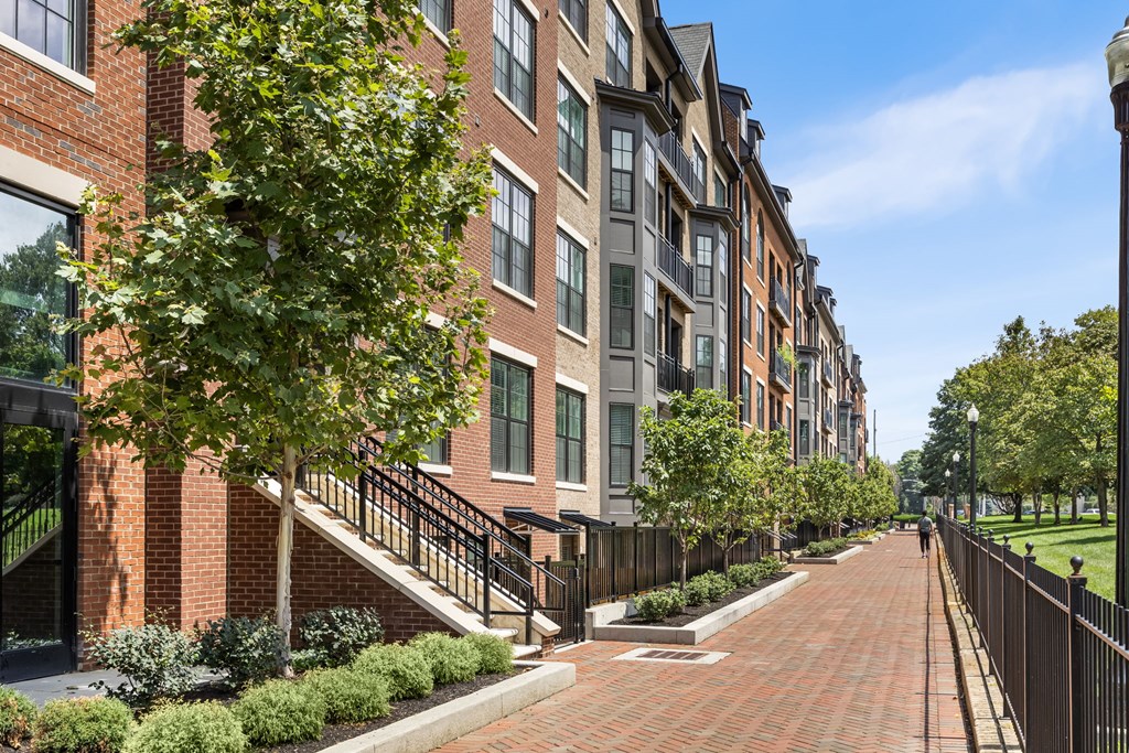 A long brick walkway leads to a building with a black fence on one side.