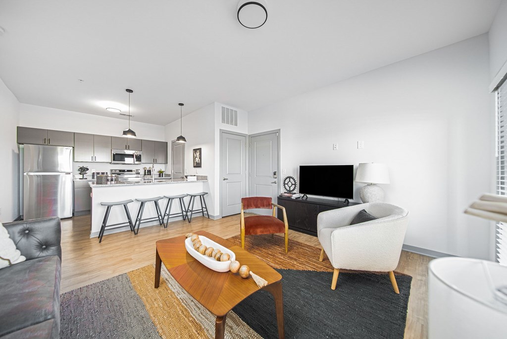 A modern living room with a white sofa, a wooden coffee table, and a kitchen area in the background.