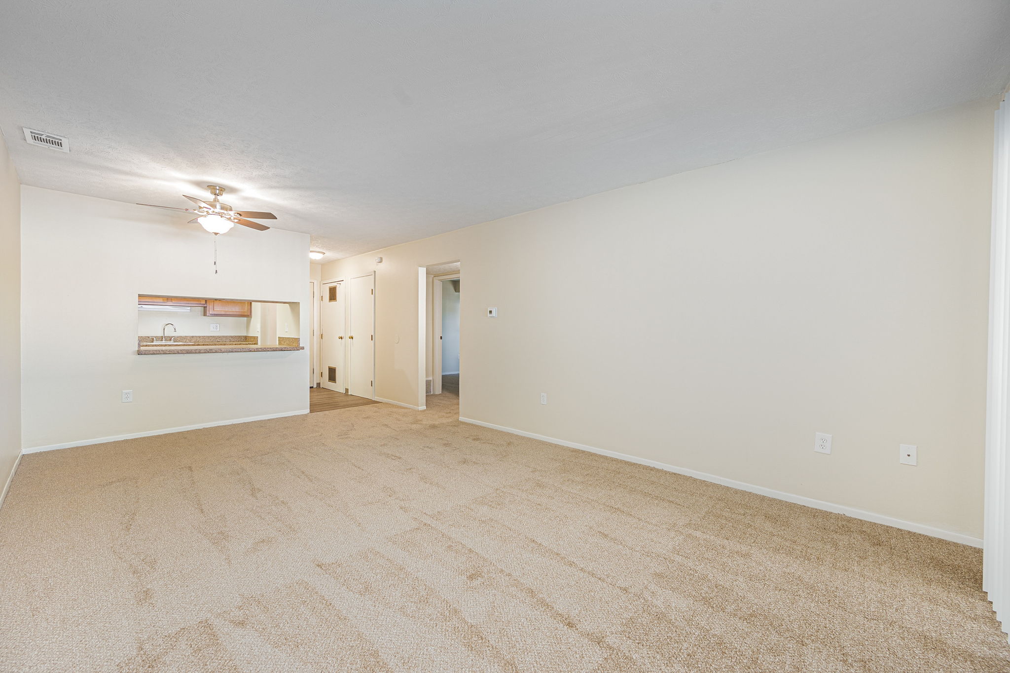 a spacious living room with carpet and a ceiling fan