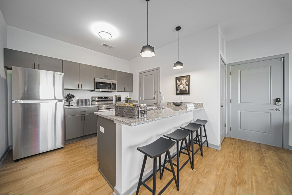 A kitchen with a refrigerator, stove, and bar stools.