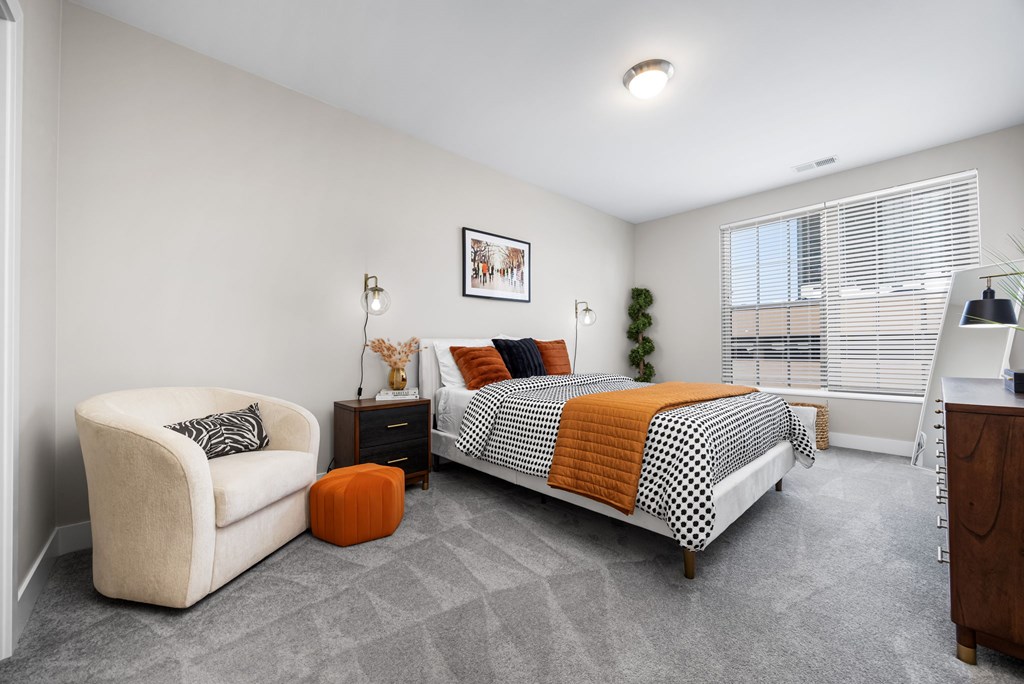 A bedroom with a bed, chair, and nightstand.