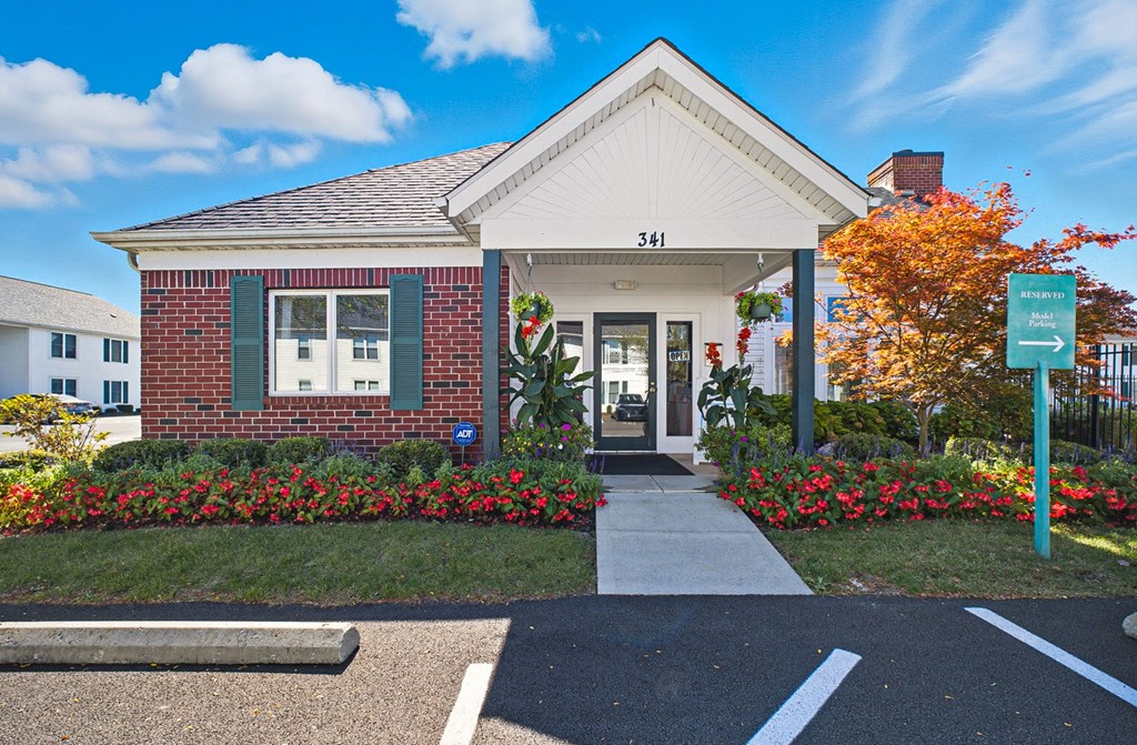 A small brick building with a white roof and a sign that reads 341 is surrounded by flowers and a clear blue sky.