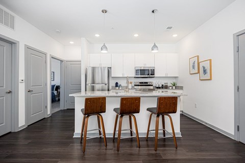 A kitchen with white cabinets and a white island with two bar stools.