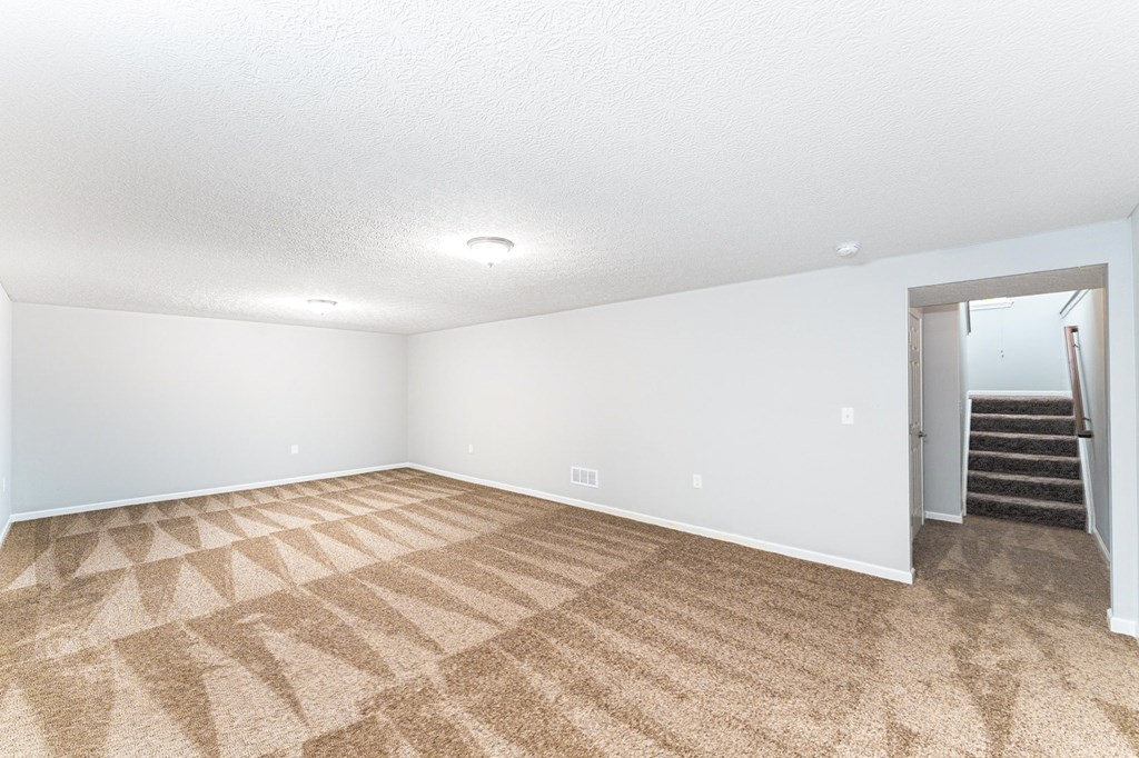 A room with a carpeted floor and a staircase in the background.