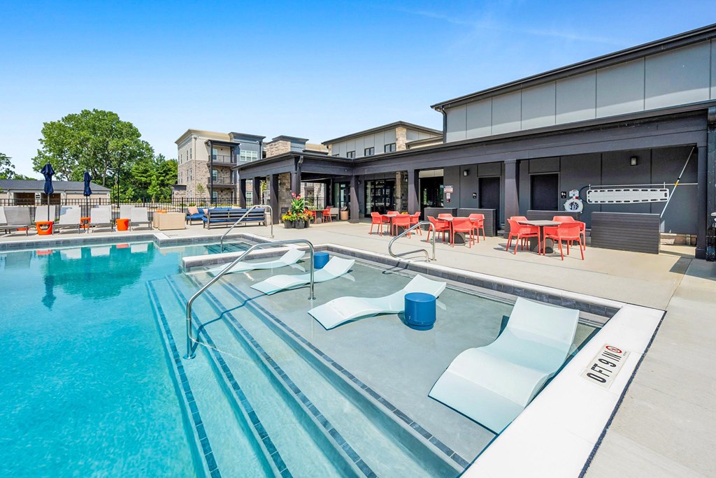 A large outdoor swimming pool with a glass barrier and red chairs.