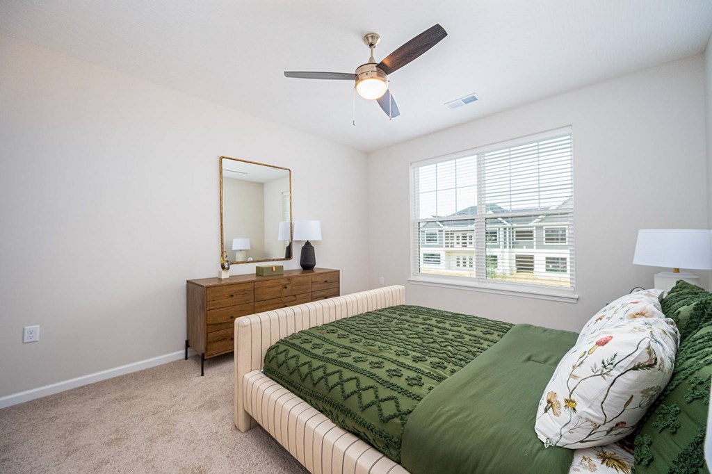 A bedroom with a bed, dresser, mirror, and window.