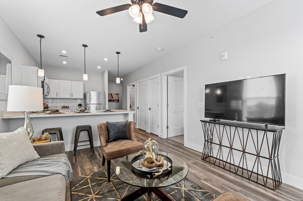 A modern living room with a grey sofa, a glass coffee table, and a television on a stand.