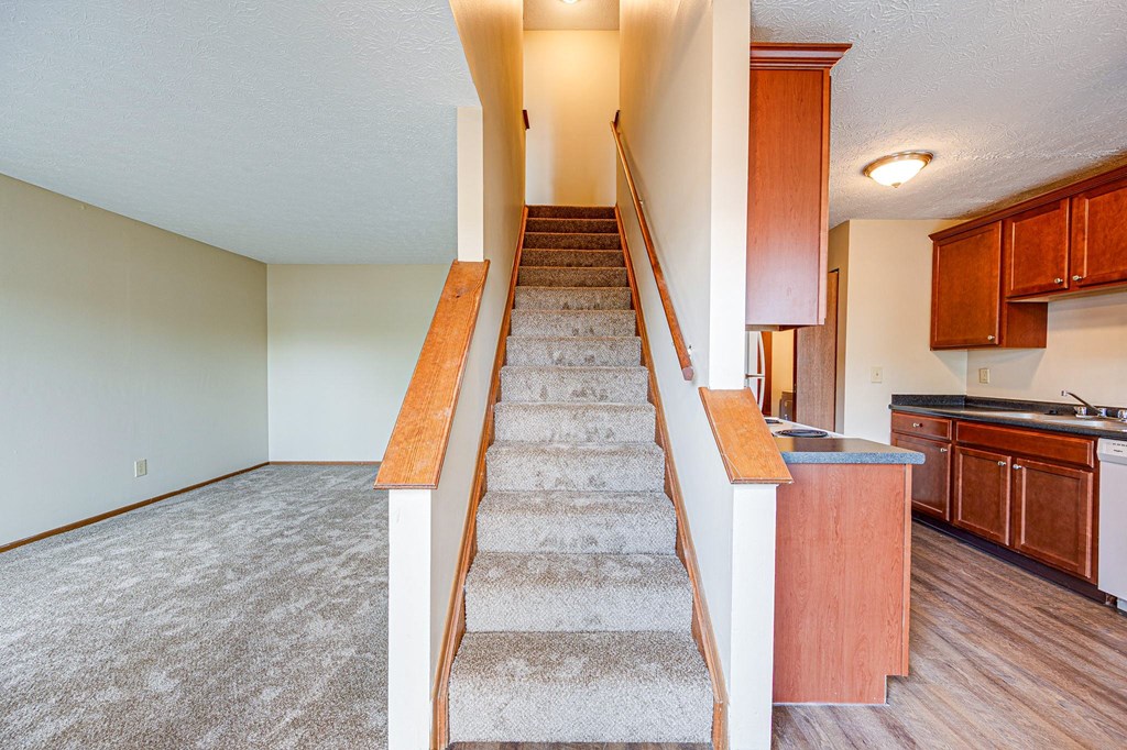 an empty living room with stairs leading up to a kitchen