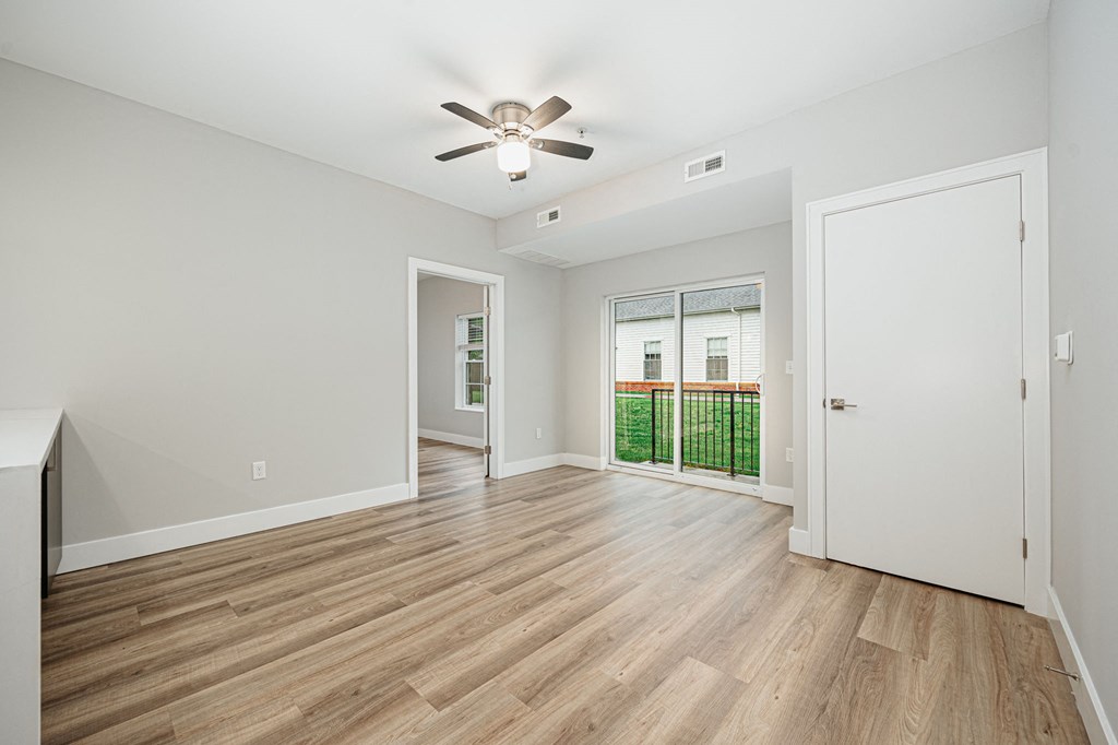 an empty living room with a ceiling fan and a door to a balcony