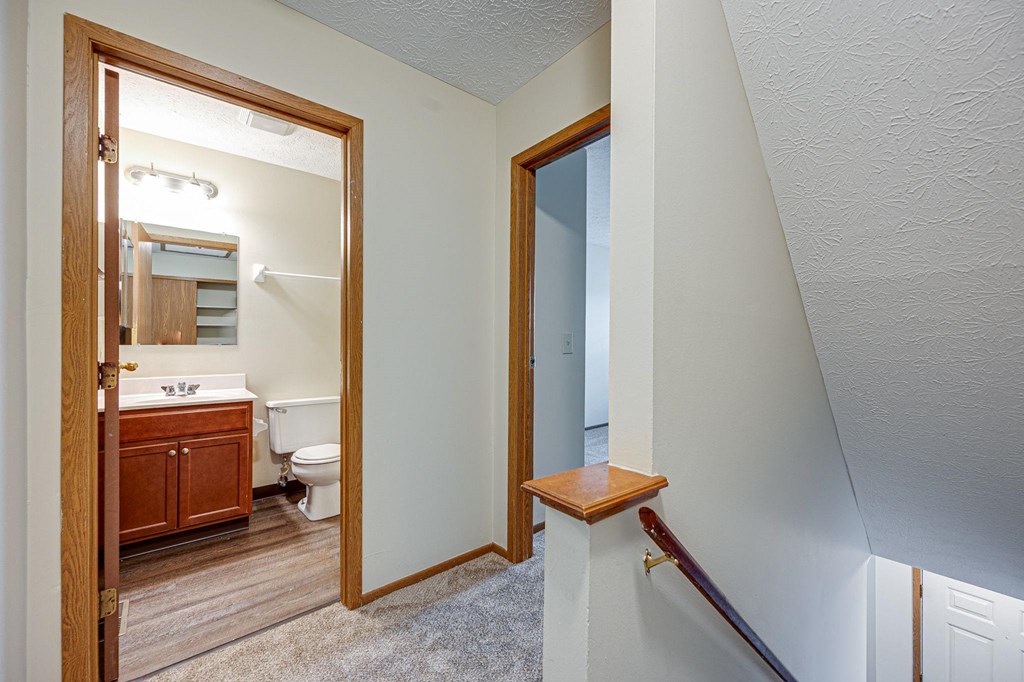 a landing leading to a bathroom with a toilet and a mirror