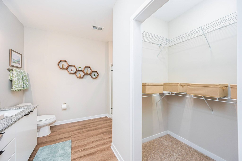 A white bathroom with a toilet, sink, and a closet with clothes hanging.