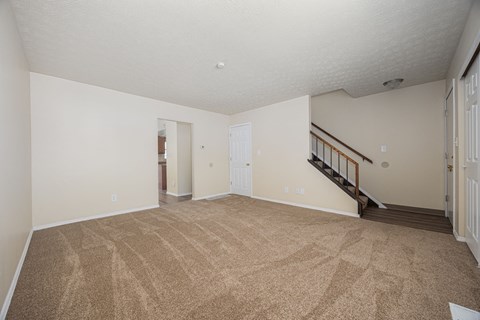 A room with a carpeted floor and a staircase.