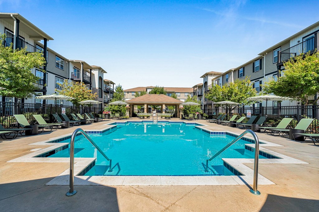 A large swimming pool surrounded by lounge chairs and umbrellas in a residential area.