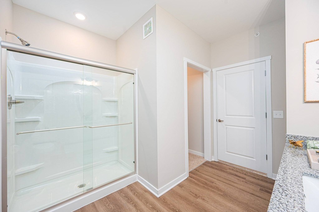 A white bathroom with a walk-in shower and a white door.
