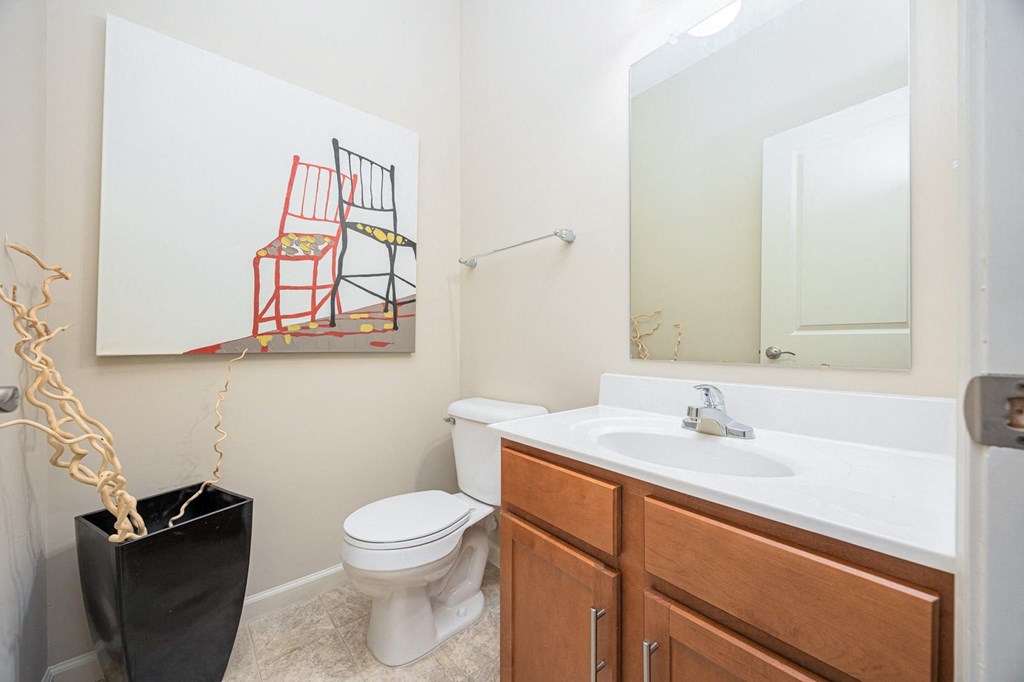 A bathroom with a toilet, sink, and a painting of a chair.