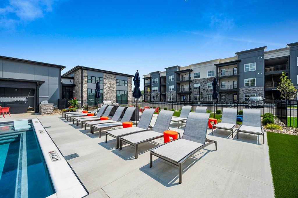 A poolside area with sun loungers and a row of apartment buildings in the background.