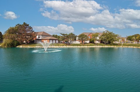 a fountain in the middle of a lake with houses in the background