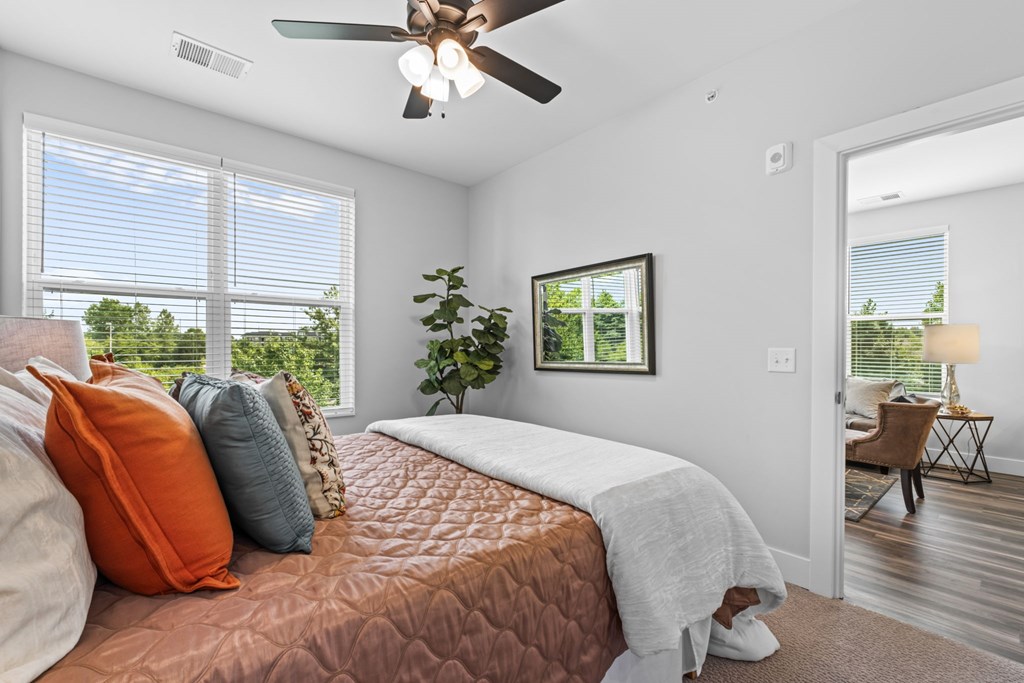 A bedroom with a bed, pillows, a ceiling fan, and a window with blinds.