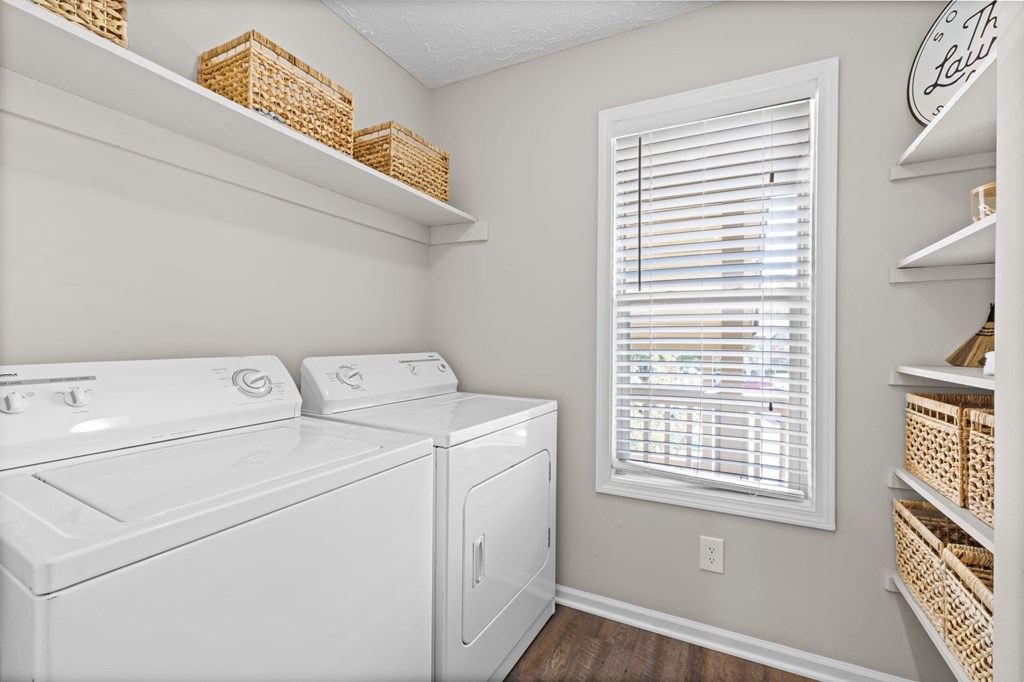A laundry room with a washer and dryer and a window with blinds.
