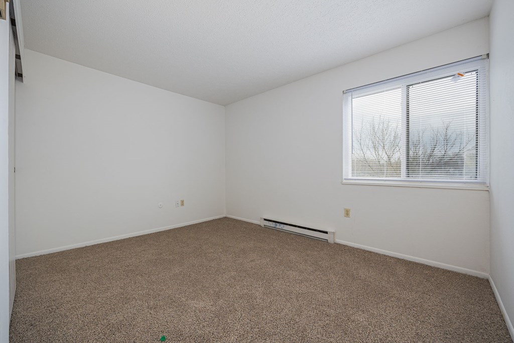 A room with a carpeted floor and a window with blinds.
