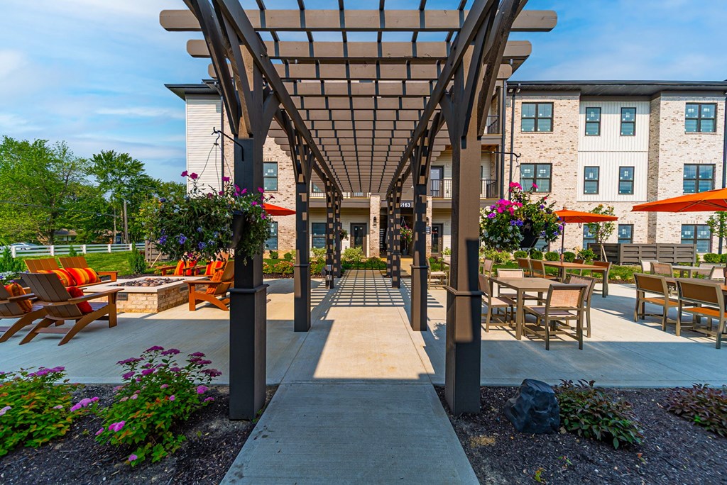 A patio with a pergola and chairs is surrounded by a building.