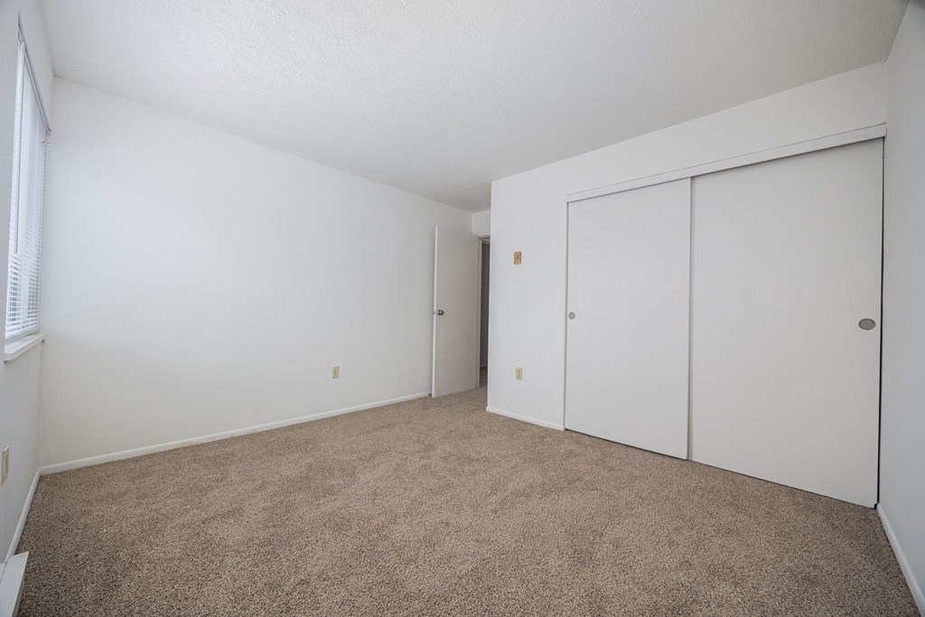 A room with white walls and carpeted floor with a window on the left.