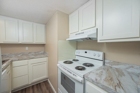 A white stove in a kitchen with white cabinets.