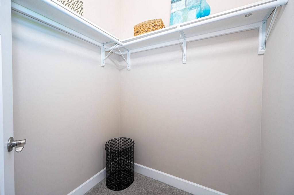a walk in closet with a white wall and a small stool