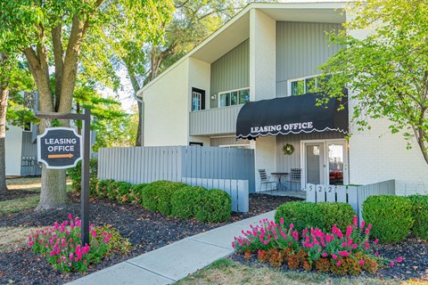 the front of a building with a leasing office sign and flowers
