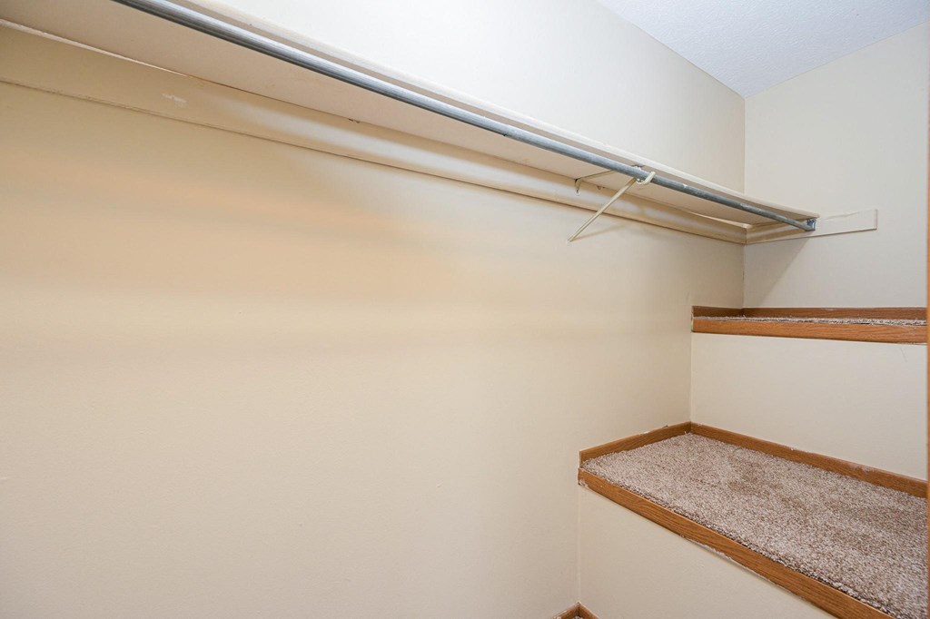a walk in closet with a white wall and a shelf on the wall