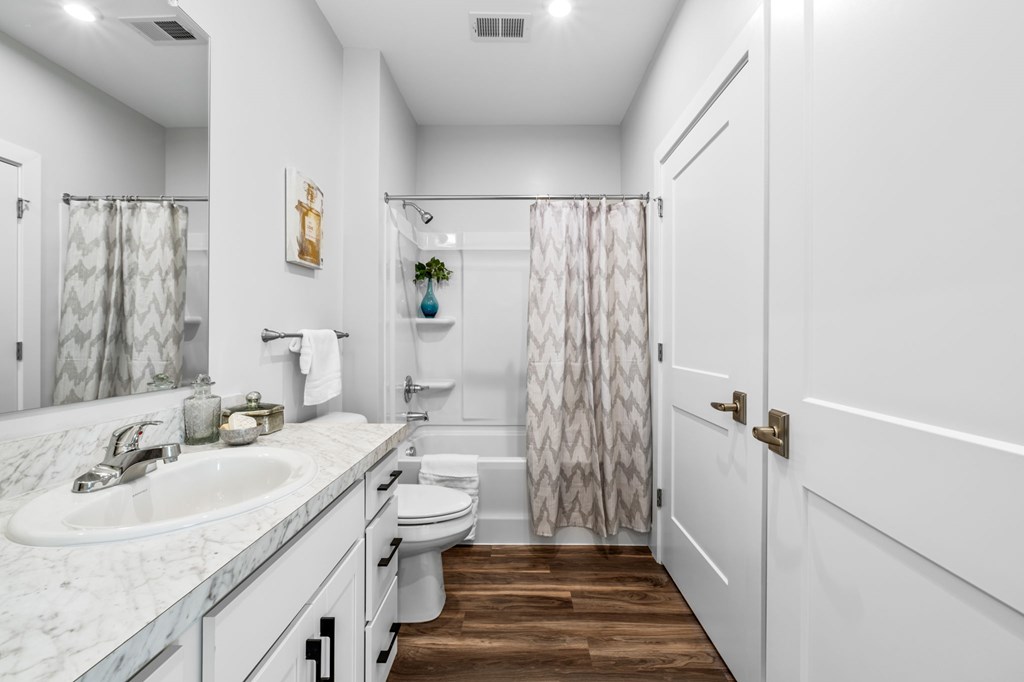 A white bathroom with a marble counter top and a wooden floor.