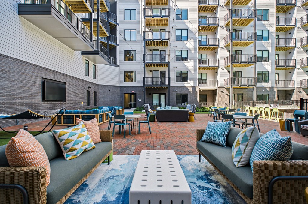 A patio area with couches and chairs in front of apartment buildings.