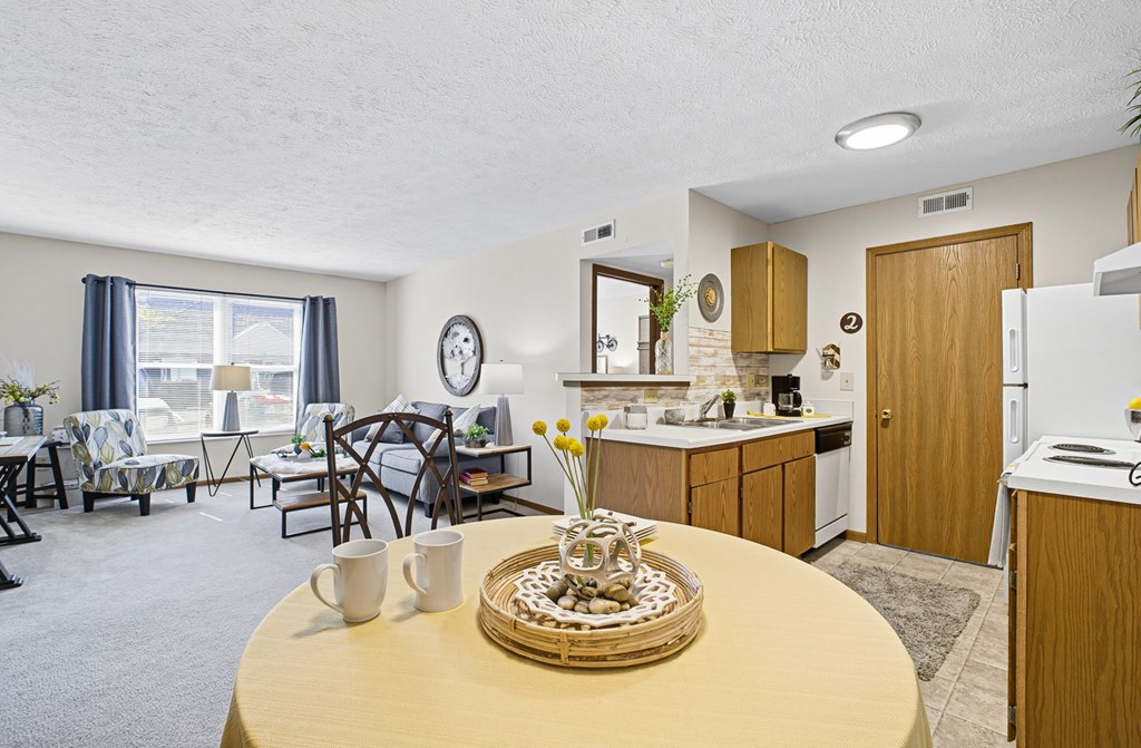 A kitchen area with a table in the middle and a dining area with chairs and a table.