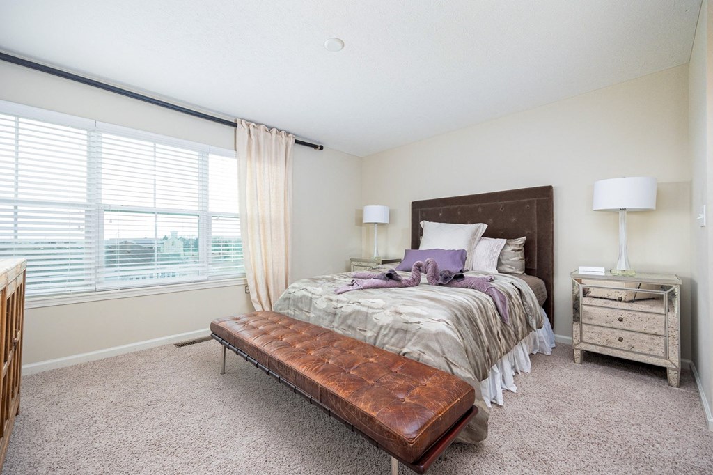 A bedroom with a bed, nightstand, and window with blinds.