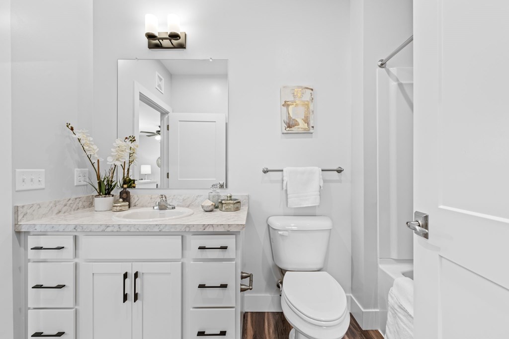 A white bathroom with a marble counter top and a toilet.