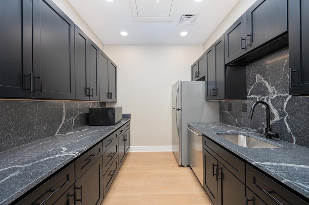A kitchen with black cabinets and a marble counter top.