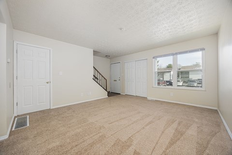 A room with a carpeted floor and a window showing a view of other buildings.