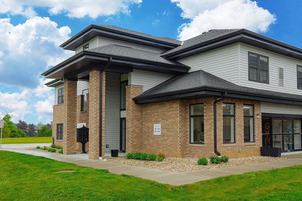 a home with brick and gray siding and a sidewalk and grass