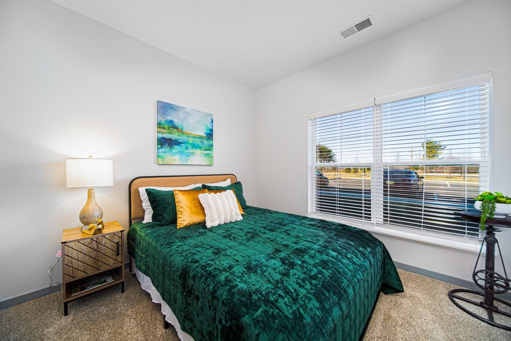 A bedroom with a green bedspread and a painting on the wall.