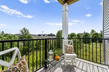 A white chair is on a porch with a table holding a lantern and a pillow.