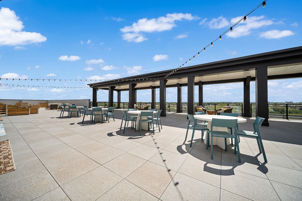 A patio with tables and chairs under a roof with string lights.