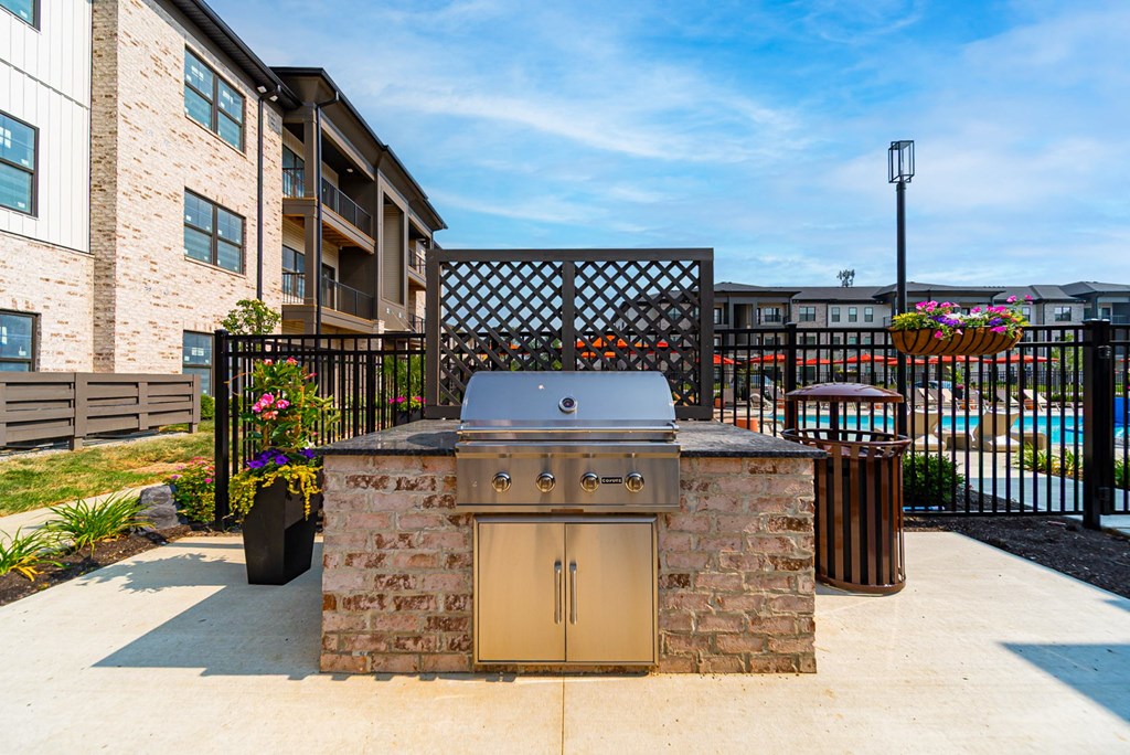 A stone BBQ grill is in the middle of a concrete patio.