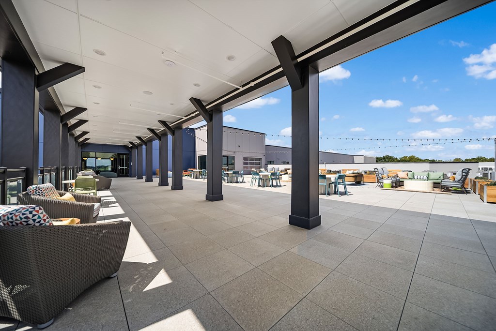 A long covered walkway with pillars and chairs on either side.